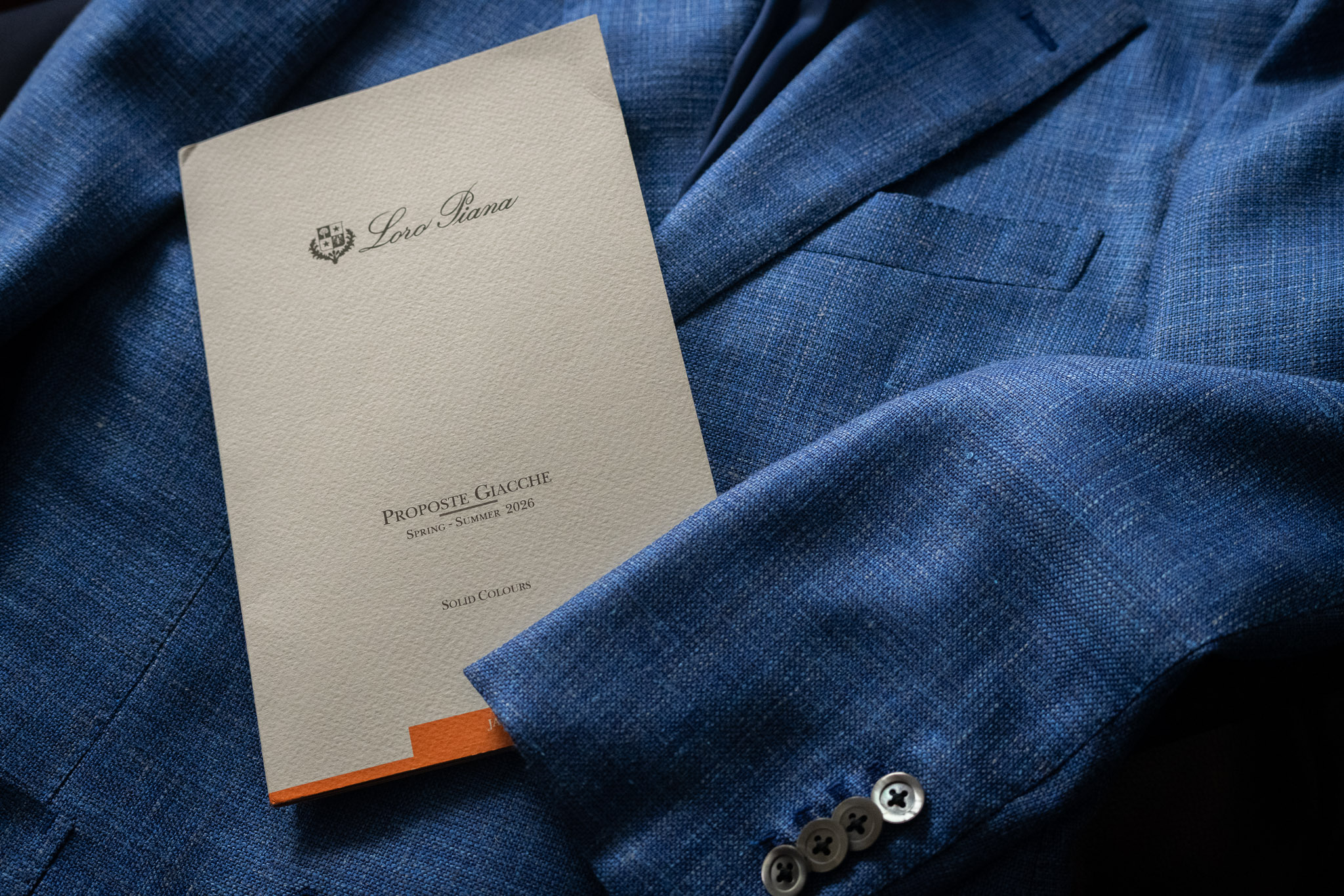 ブルーのジャケットの上に置かれたLoro Piana(ロロ・ピアーナ)2026年春夏コレクションpropsoste-giaccheの生地見本帳